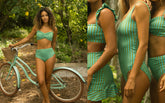 Woman in a green bikini standing next to a teal bicycle in a forest setting
