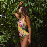 Woman wearing a yellow floral swimsuit standing against a green leafy background