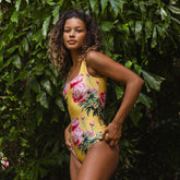 Woman wearing a yellow floral swimsuit standing against a green leafy background