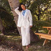 Woman in a white coverup over a two piece swimsuit standing under a palm tree in a tropical setting