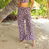 Person wearing a floral outfit standing on a sandy beach with palm trees in the background