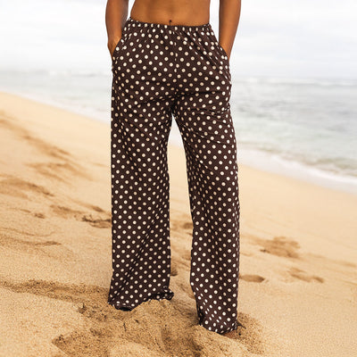Person wearing black polka dot pants standing on a sandy beach.