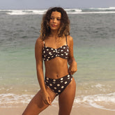 Woman in a polka dot bikini standing on a beach with ocean waves in the background
