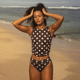 Woman in a polka dot swimsuit standing on a beach with ocean waves in the background