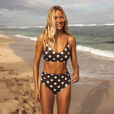 Woman in a polka dot bikini standing on a beach with ocean waves in the background