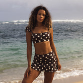 Woman in a polka dot bikini standing on a beach with ocean in the background
