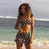 Woman in a polka dot swimsuit standing on a beach with ocean waves in the background