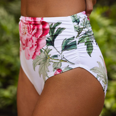 Floral high-waisted bikini bottom with pink flowers and green leaves on a white background.