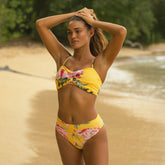 Woman in a yellow floral bikini standing on a beach