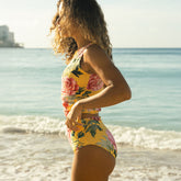 Woman in a floral swimsuit standing on a beach with ocean in the background