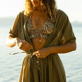 Woman wearing a zebra print bikini top and green cover-up by the water