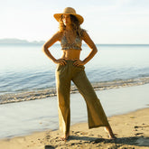 Woman in a bikini and beach pants standing on a beach with ocean in the background