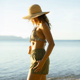 Woman in a bikini and hat standing on a beach with ocean in the background