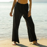 Woman wearing black wide-leg linen pants standing on a beach.