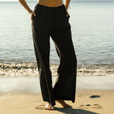 Woman wearing black wide-leg pants as a swimsuit cover up standing on a beach with ocean in the background