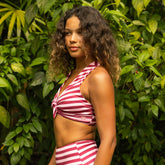 Side view of a woman in a magenta stripe top knot bikini top and high waisted bottoms in a tropical setting