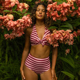 A woman wearing a striped two piece swimsuit with high waisted bikini bottoms standing in a tropical setting