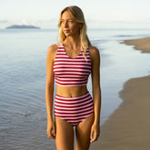 Woman wearing a pink striped swimsuit standing on a beach.