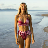 Women's triangle bikini top in cranberry stripe with peplum bikini bottoms walking on tropical beach.