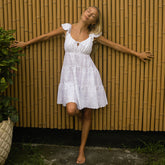 Woman in a white eyelet cover-up dress standing against a bamboo fence