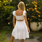 Woman in an open back dress in white lace material standing in a garden with greenery and flowers.