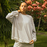 Woman wearing a striped long-sleeve tee standing in a garden with greenery and flowers.