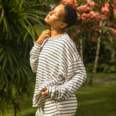 Woman in a striped matching pajama set standing in a garden with greenery and flowers.