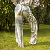Back view of woman wearing navy and white striped pants standing on grass with greenery in the background