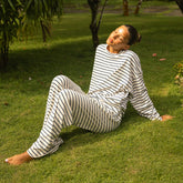 Woman wearing a navy and white striped pajama set sitting on grass
