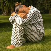 Woman sitting in the grass wearing a matching pajama set in navy blue stripes. 