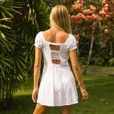 Back view of woman in an open back white dress walking through a garden with greenery and flowers.