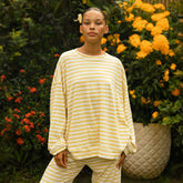 Woman wearing a yellow and white striped long sleeve tee with matching lounge pants standing in front of flowers
