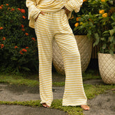 Woman wearing yellow and white striped wide-legged lounge pants standing outdoors with plants in the background