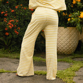 Woman wearing yellow and white striped pajama pants standing outdoors with plants in the background