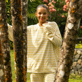Woman in yellow striped matching set standing among trees in a garden
