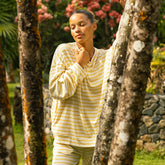 Woman in a yellow shirt standing between two trees in a garden.