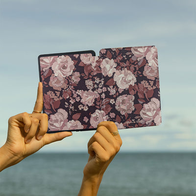 Floral-patterned case held up against a sky and water background
