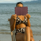 Person in polka dot bikini sitting on a beach chair with a polka dot kindle case covering their face.