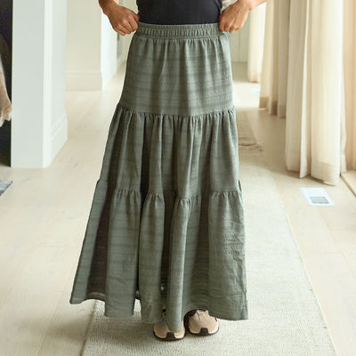 Woman wearing a long green, summery maxi skirt in a minimal indoor setting