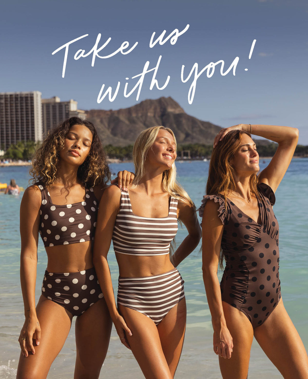 Three women in swimsuits on a beach with a mountain in the background