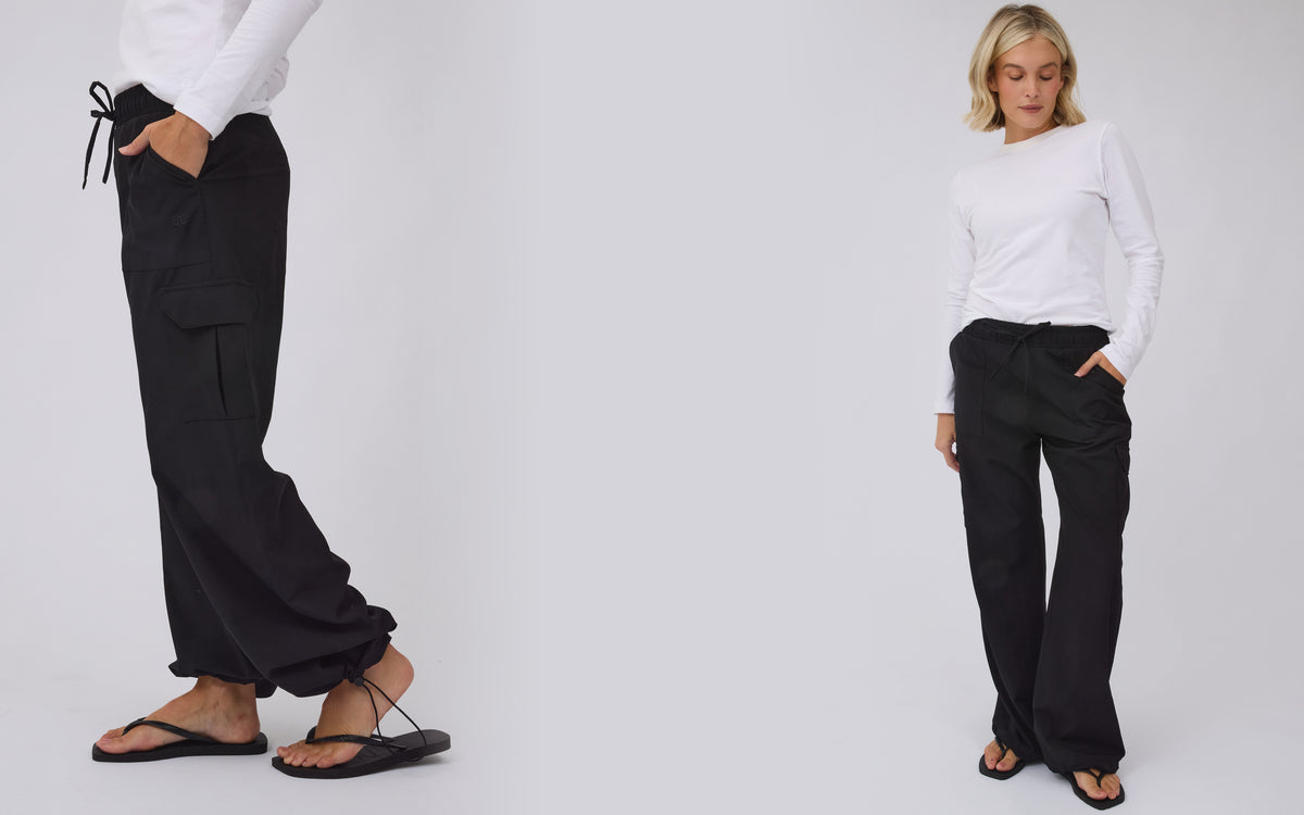 A model wearing black wide-leg cargo pants with a drawstring waist, styled with a white long-sleeve top and black sandals, shown in a full-body shot and a cropped side-profile view against a light gray studio background.