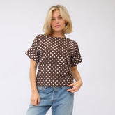 Woman wearing a brown polka dot shirt and blue jeans on a white background