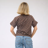 Person wearing a brown polka dot shirt and blue jeans on a white background