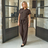 Woman in a polka dot jumpsuit standing in a modern interior setting with large glass doors.