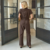 Back view of a woman in a polka dot flattering jumpsuit standing in a modern interior setting with large glass doors.