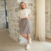 Woman in a perfect white t-shirt and striped skirt standing against a stone wall.
