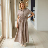 Woman wearing a short sleeved maxi dress in brown gingham standing in a bright room.