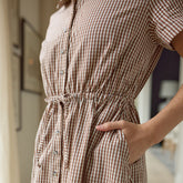 Close up view of a brown and white gingham dress worn by a person with a blurred background
