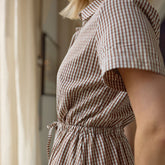 Close up of woman wearing a brown and white gingham dress with short sleeves. 