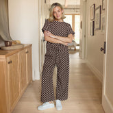 Woman wearing a cute matching set—brown polka dot pants and a brown polka dot top in a hallway. 